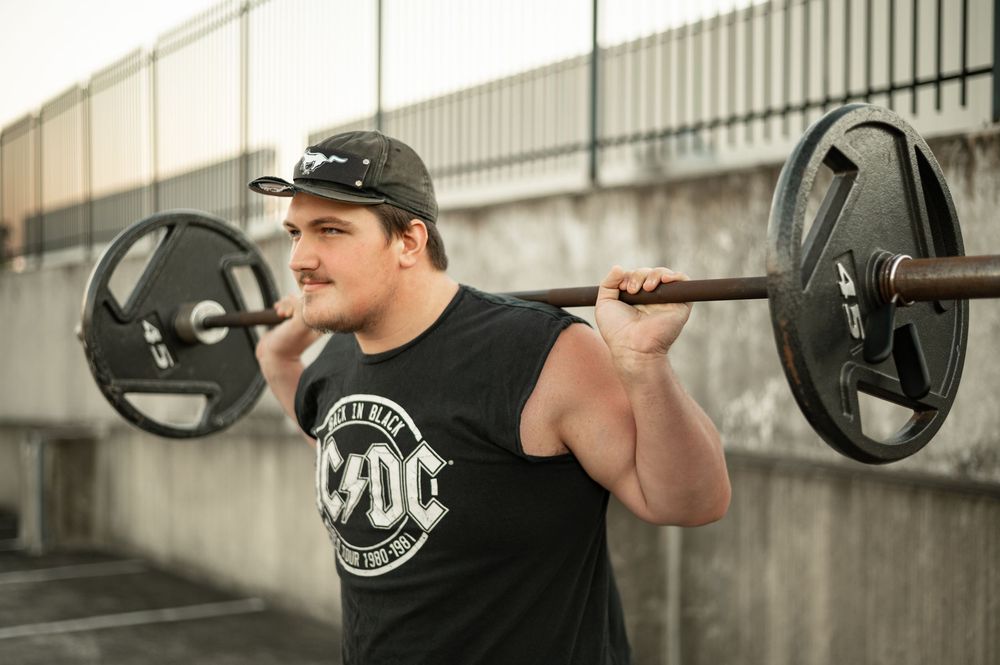 Person performing a barbell back squat exercise with proper form in a gym setting.