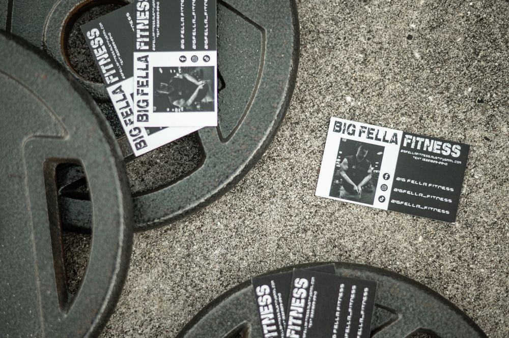 Black and white weight plates and business cards scattered on a textured concrete surface create a gritty fitness scene.