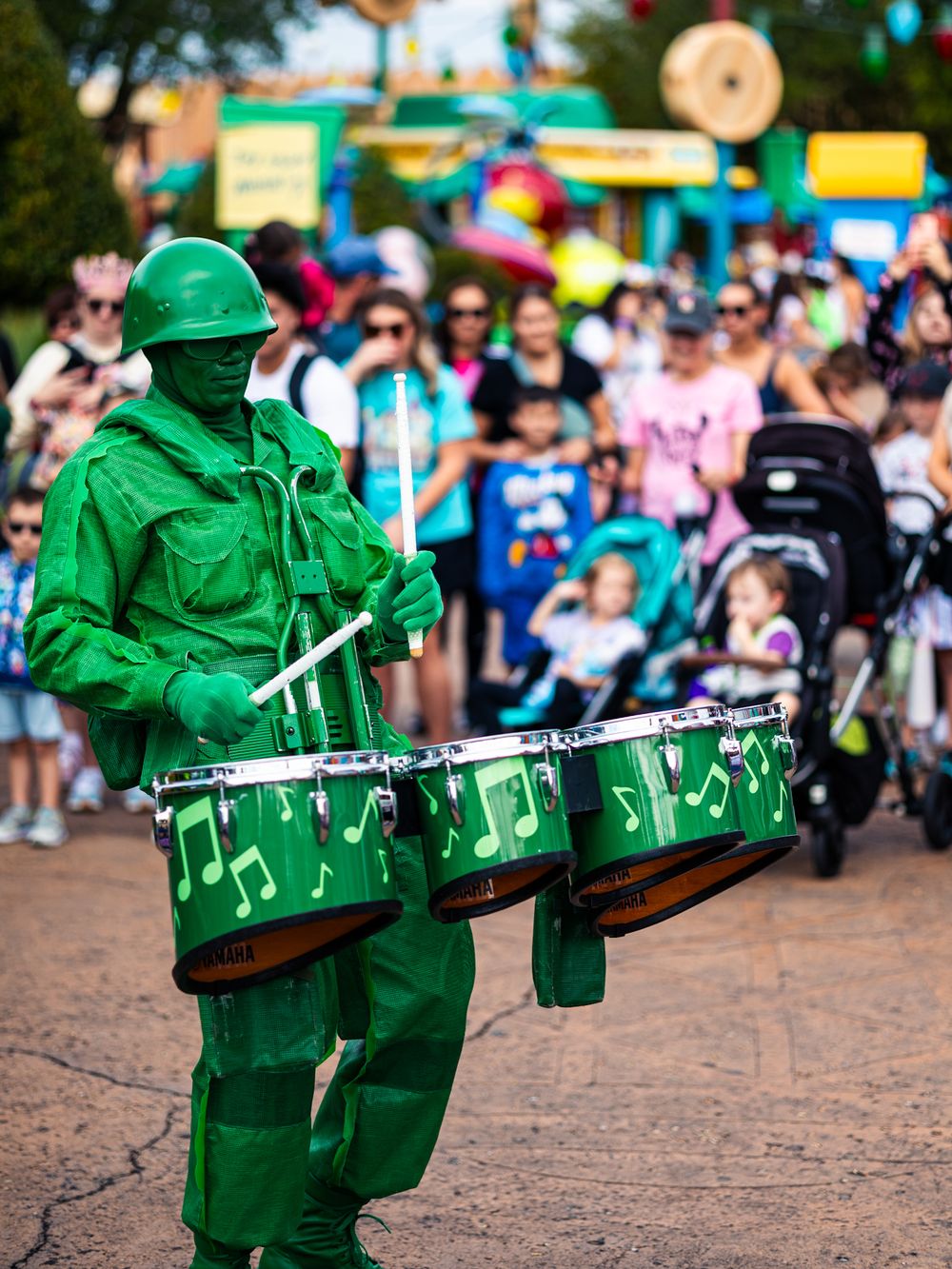 Green toy soldiers with musical note decorations march in formation at a theme park parade.