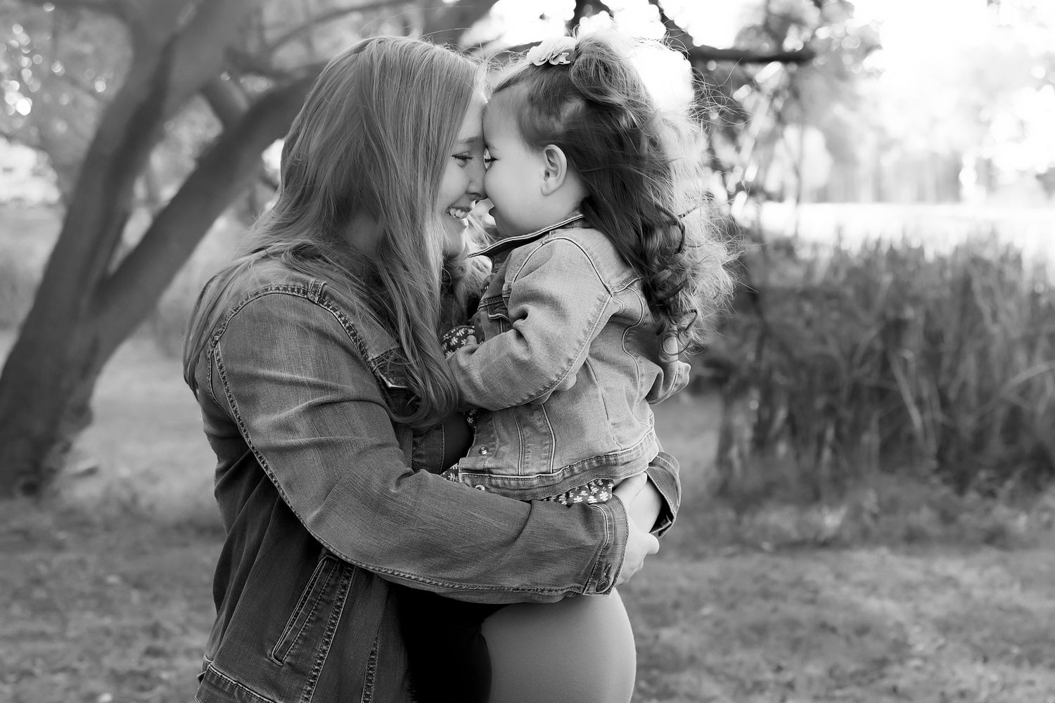 Black and white photograph of two young children whispering and sharing a sweet moment in matching dresses.