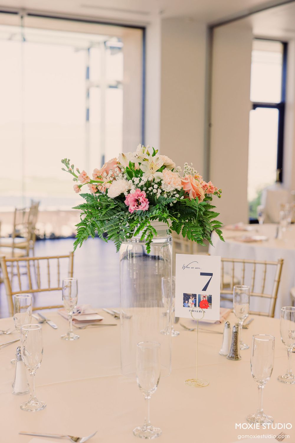 Elegant wedding reception tables set with white linens, gold chiavari chairs, and delicate floral centerpieces.