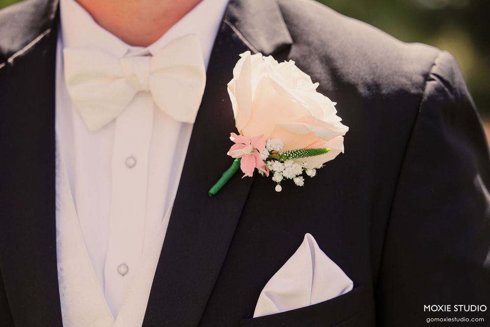 A row of groomsmen wearing black tuxedos with white boutonnieres lined up at a formal wedding ceremony.