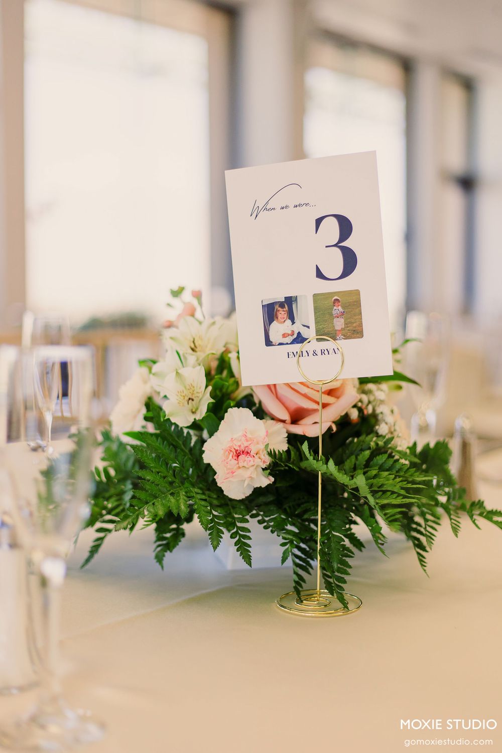 Elegant wedding table centerpiece with pink and white flowers, greenery, and table number cards.