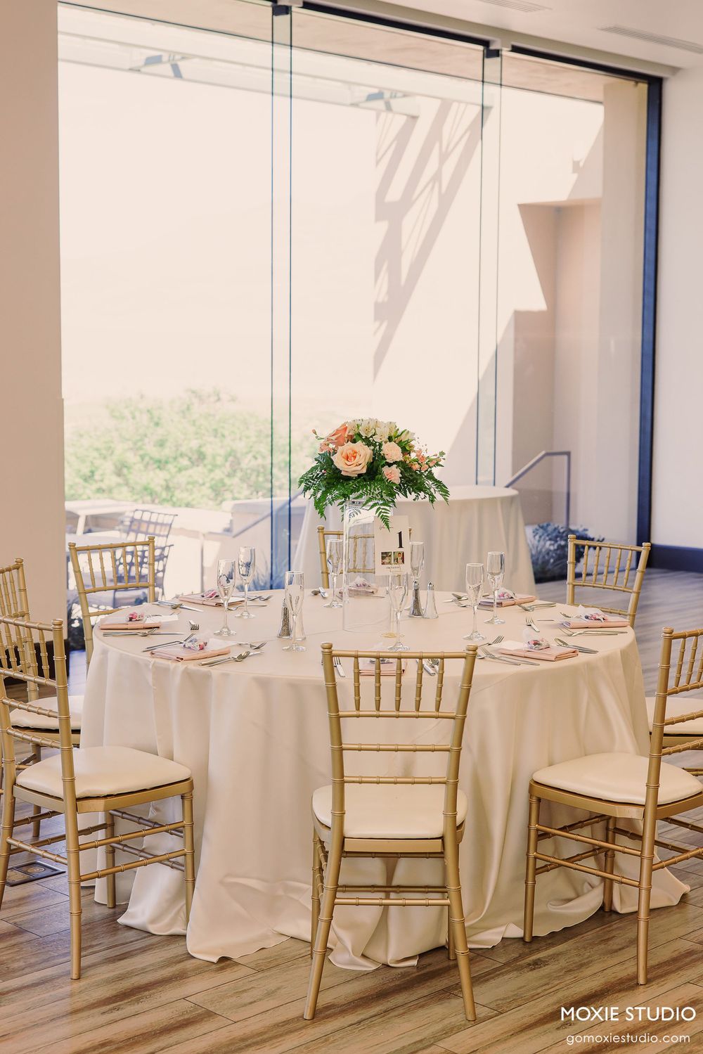 Elegant wedding reception venue with white tablecloths and gold chiavari chairs set up for a formal dining event.