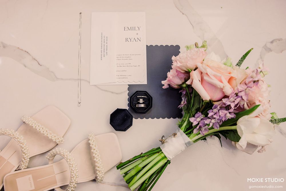 Pink and white floral wedding bouquets and invitation cards arranged on a light beige textured surface.