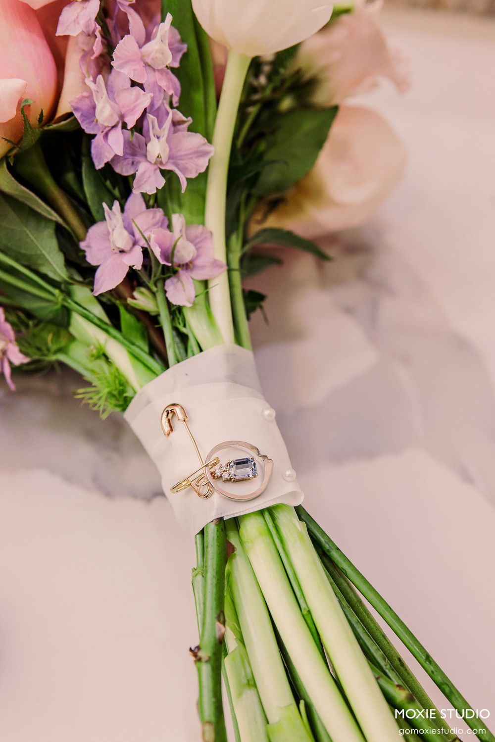 Wedding rings nestled among pink and purple flowers in an elegant floral bouquet arrangement.