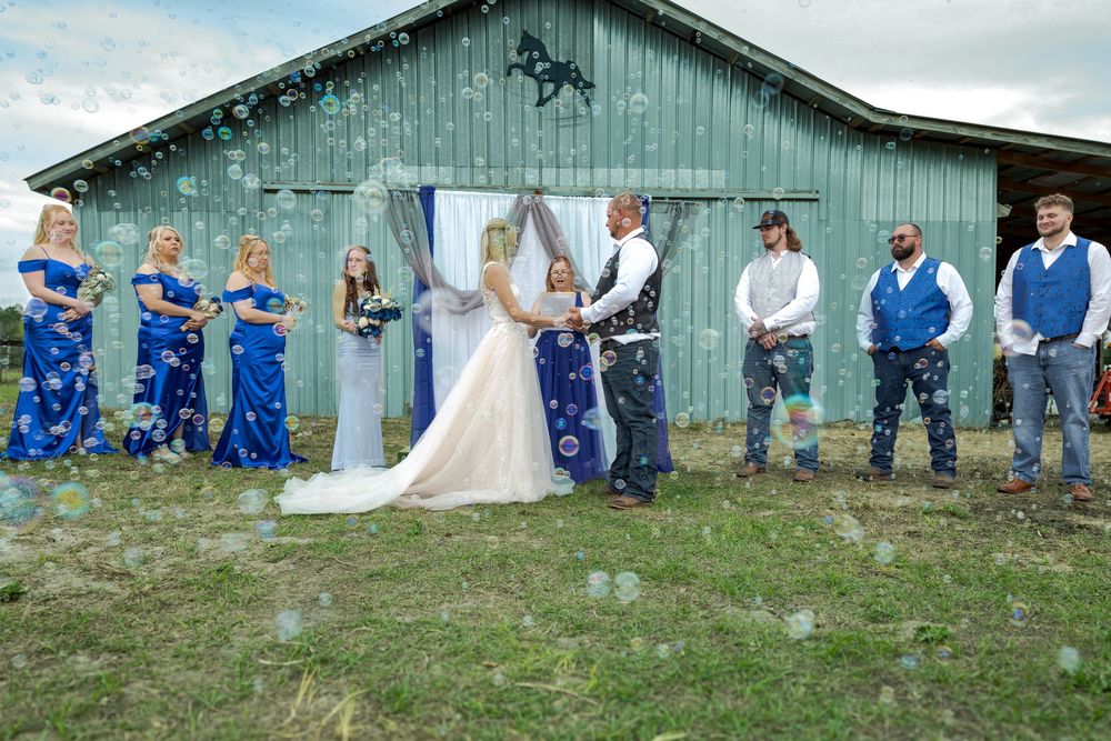 Bride and groom ceremony at rustic barn venue with wedding party and confetti bubbles.