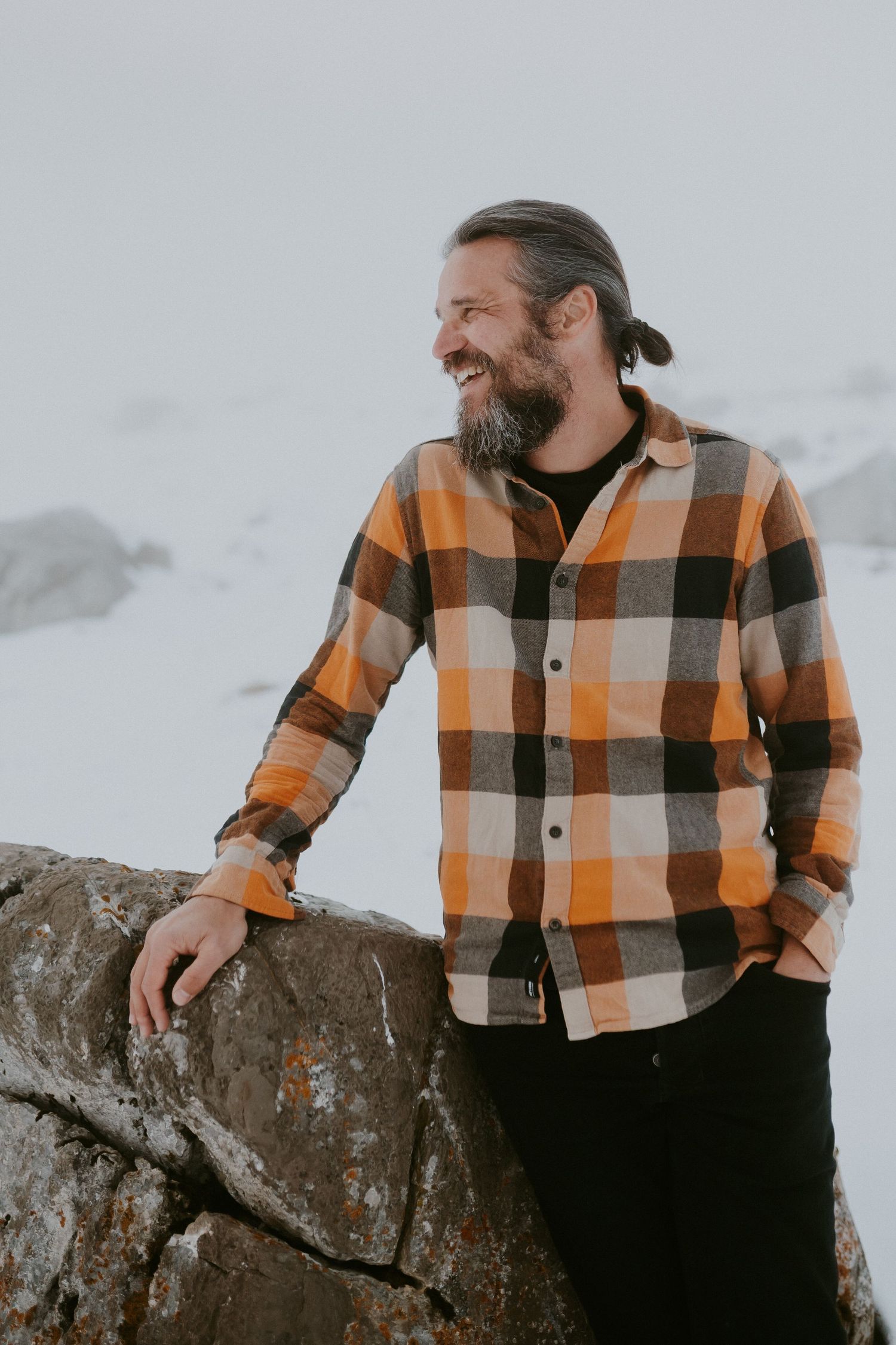 Person in black sweater sits thoughtfully among rocks and wildflowers during golden hour.