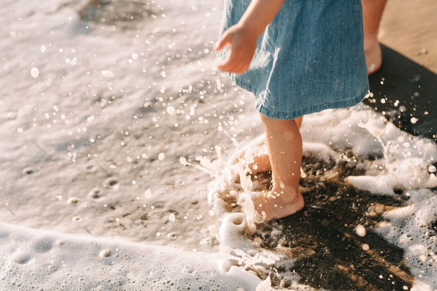 Little feet on a sandy shore during a family lifestyle session. Photograph of kids running in and out of the water