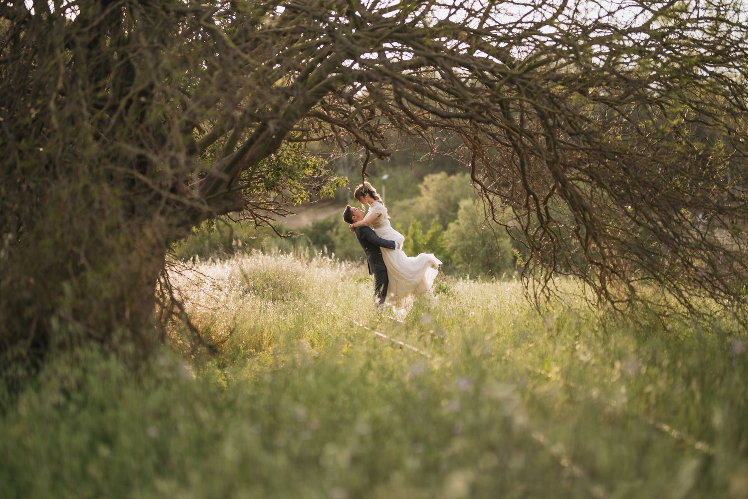 Wedding photo in natural meadow setting with white dog under arching tree branches.