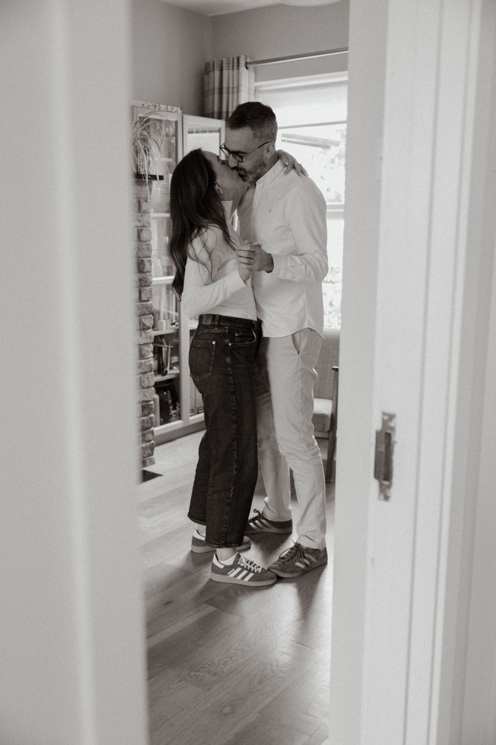 A romantic black and white photo of a couple sharing an intimate moment in a doorway at home.