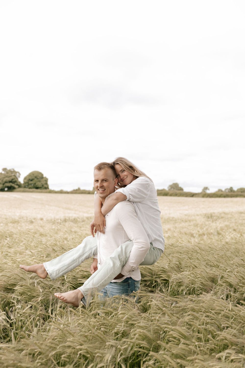 A couple in white clothing sits together affectionately in a golden wheat field on a bright summer day.