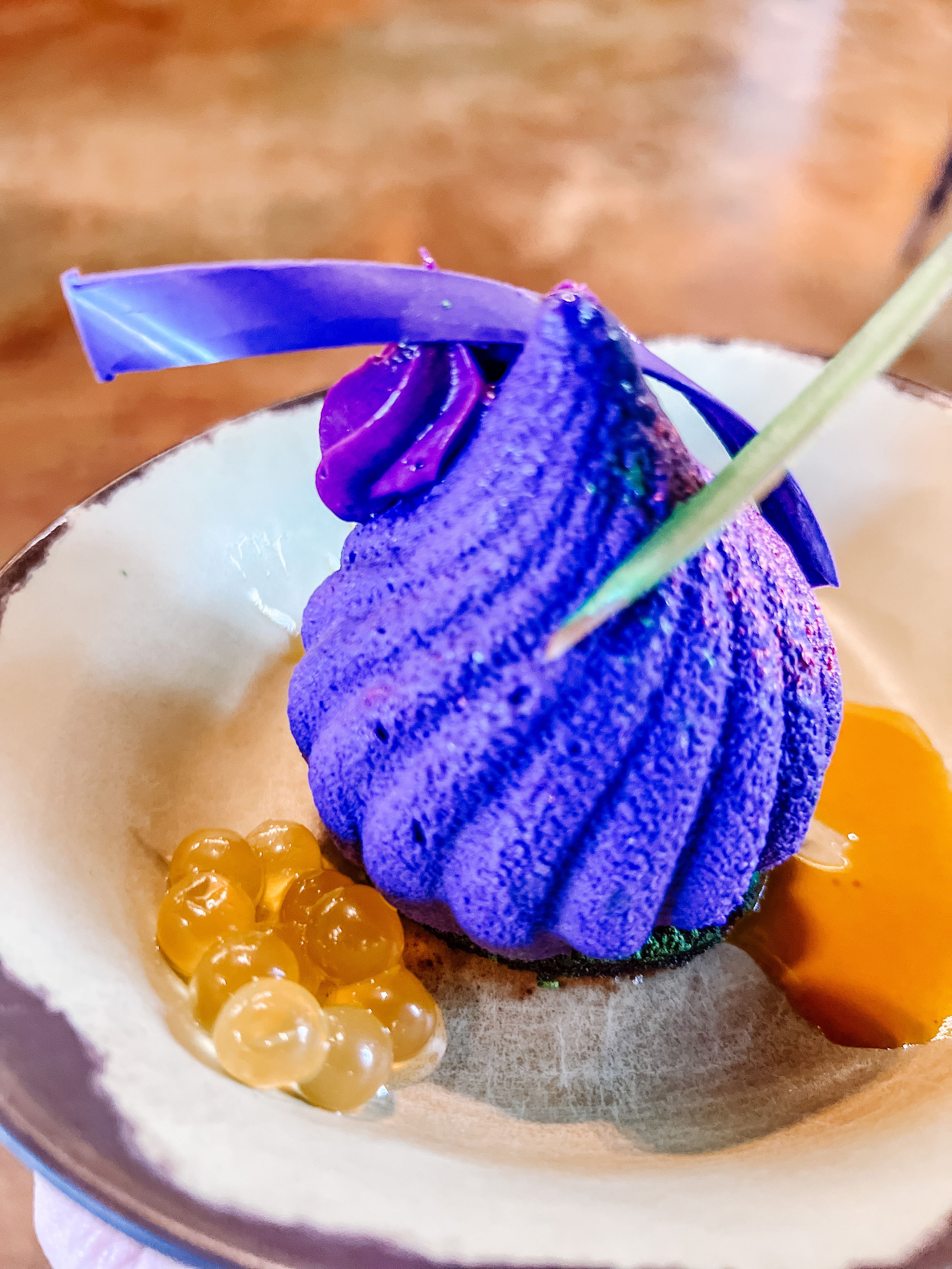 A vibrant purple swirled dessert served with orange boba pearls in an elegant white ceramic bowl.