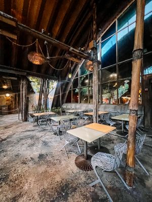 Rustic restaurant interior with wooden beams, hanging lights, and metal cafe tables in a dimly lit space.