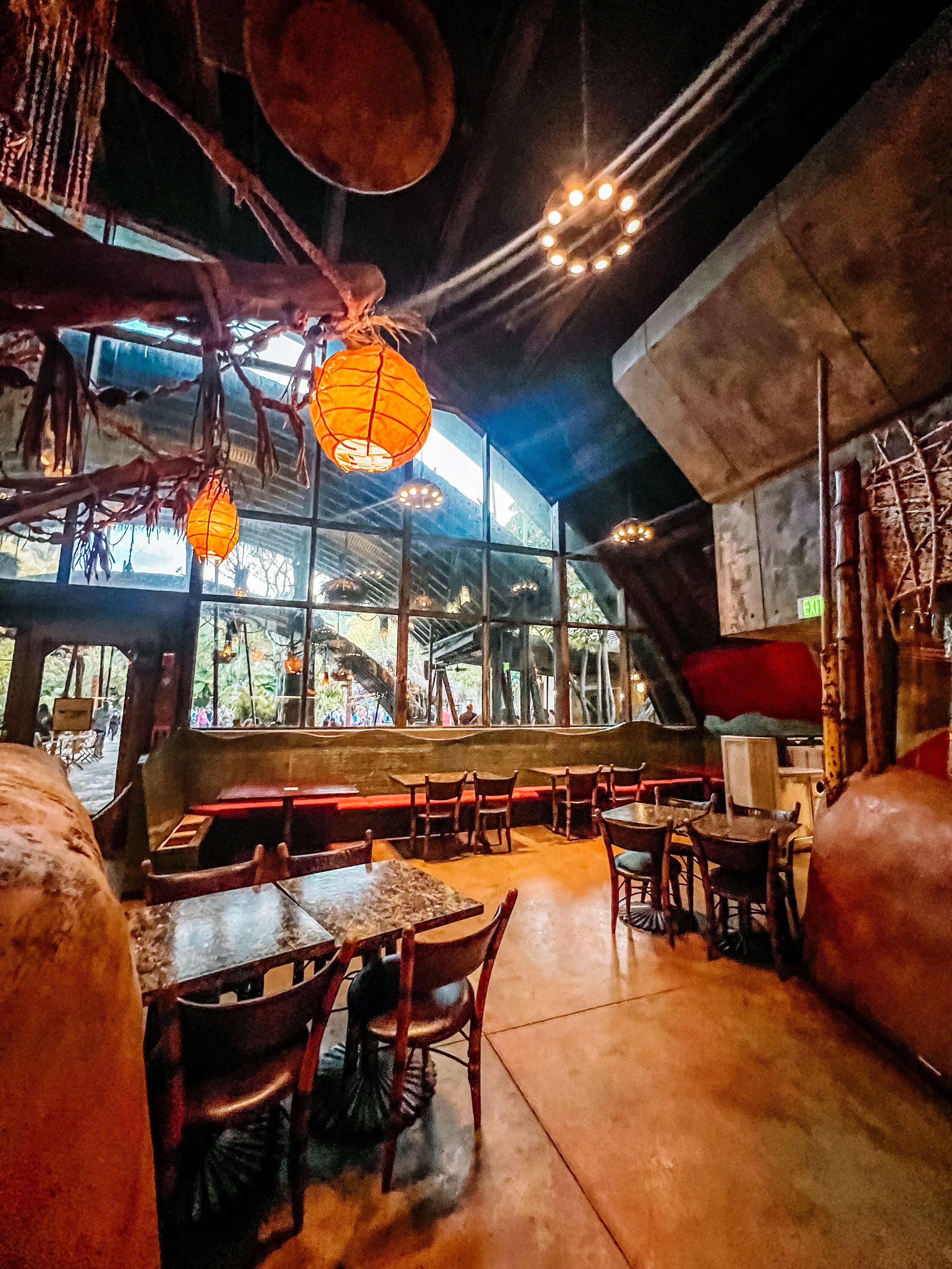 Dark atmospheric bar interior with red lighting, exposed ductwork, and vintage decor showing multiple connected seating areas.