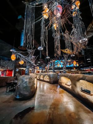 Dark spooky bar interior with vintage chandeliers and spider web decorations creating an eerie Halloween atmosphere.