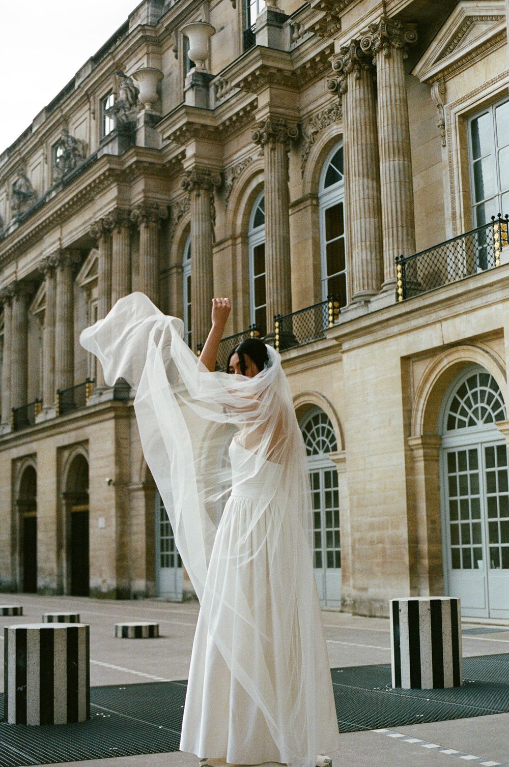 A dramatic shot of a flowing white dress billowing in front of a grand historic building with ornate architecture.