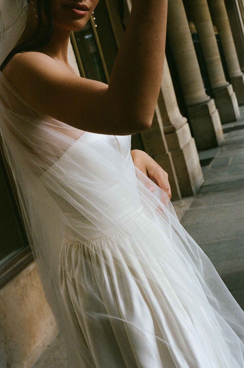 A person in a flowing white dress leans against ornate stone pillars in dramatic lighting creating an ethereal mood.