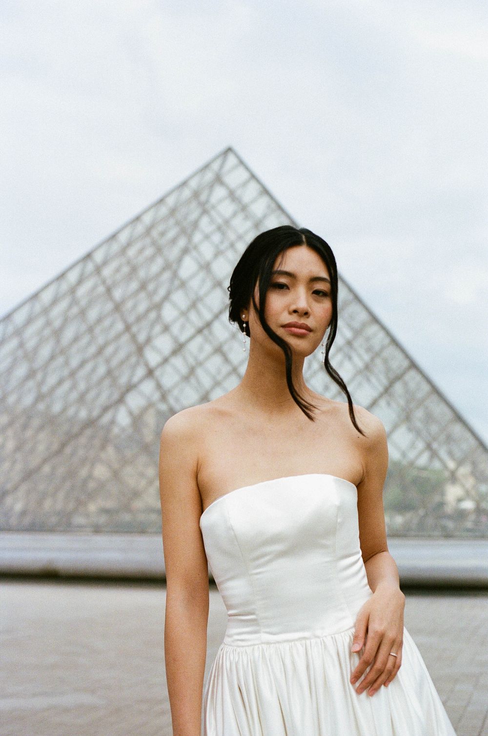 A modern bridal portrait framed by the geometric glass pyramid of the Louvre museum.