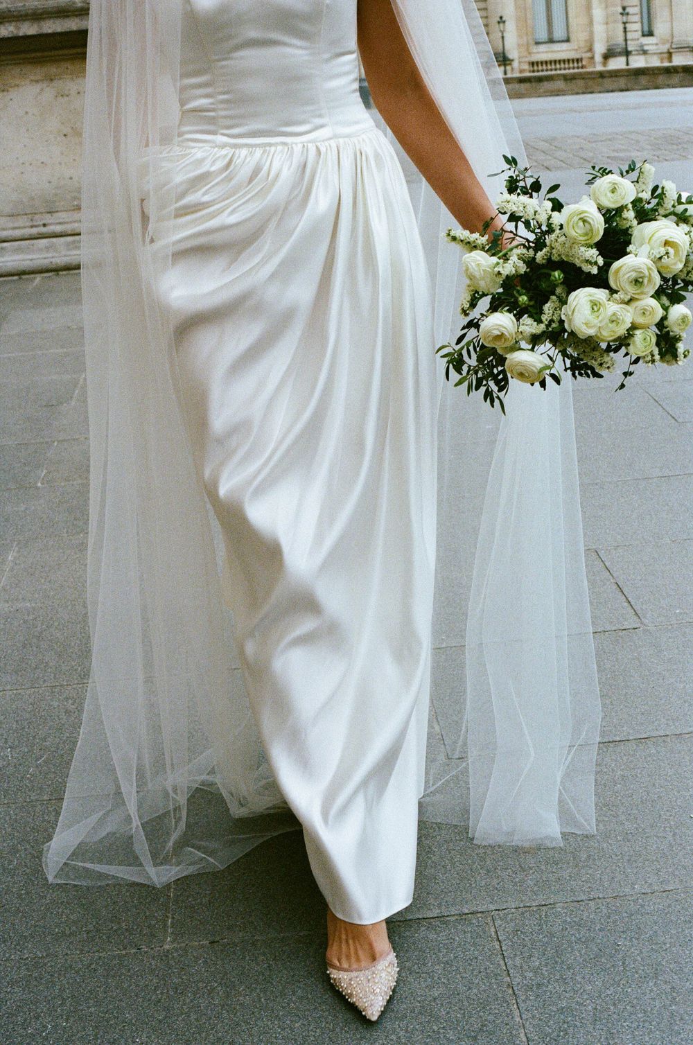 Close up view of a bride in a white wedding dress holding an elegant white and green floral bouquet.