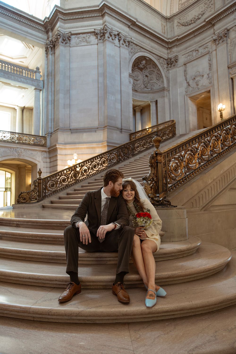 Couple sitting on ornate marble staircase in elegant historic building interior.