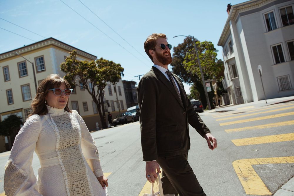 Couple walking down sunny street with white buildings in urban setting.