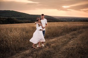 A couple in white dances together in a golden field at sunset with rolling hills in the background.