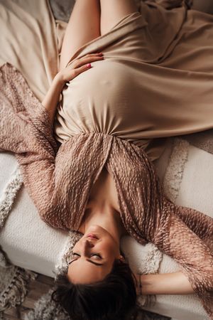 Overhead view of someone lying on beige bedding with flowing fabric and textured blankets in warm neutral tones.