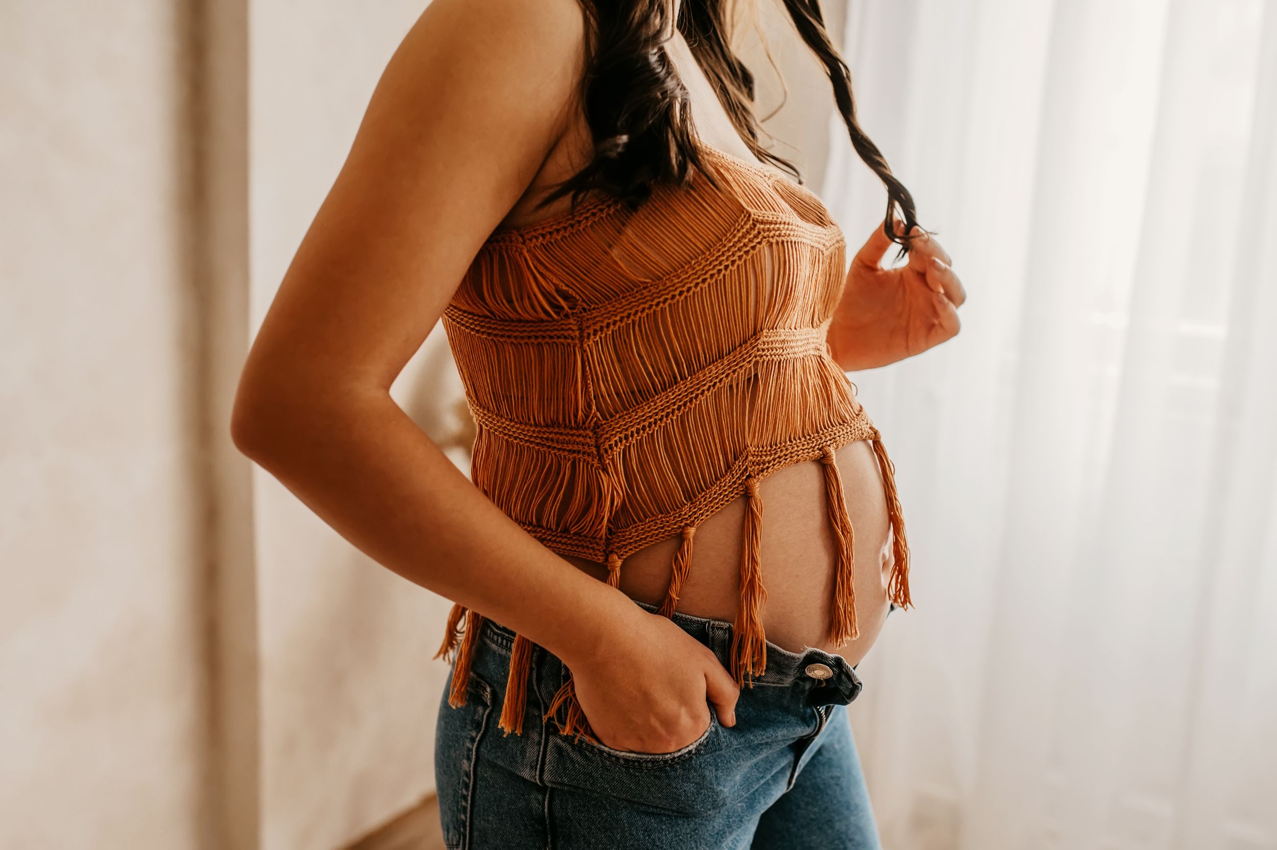 Cropped view of a brown fringe suede crop top paired with blue jeans against a white backdrop.
