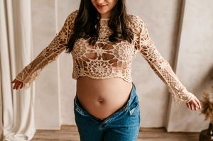 Person wearing a cropped lace long sleeve top with denim jeans poses against a light curtain background.