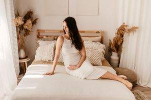 A person in a white dress relaxes on a cozy bed with pampas grass decor and natural sunlight streaming in.