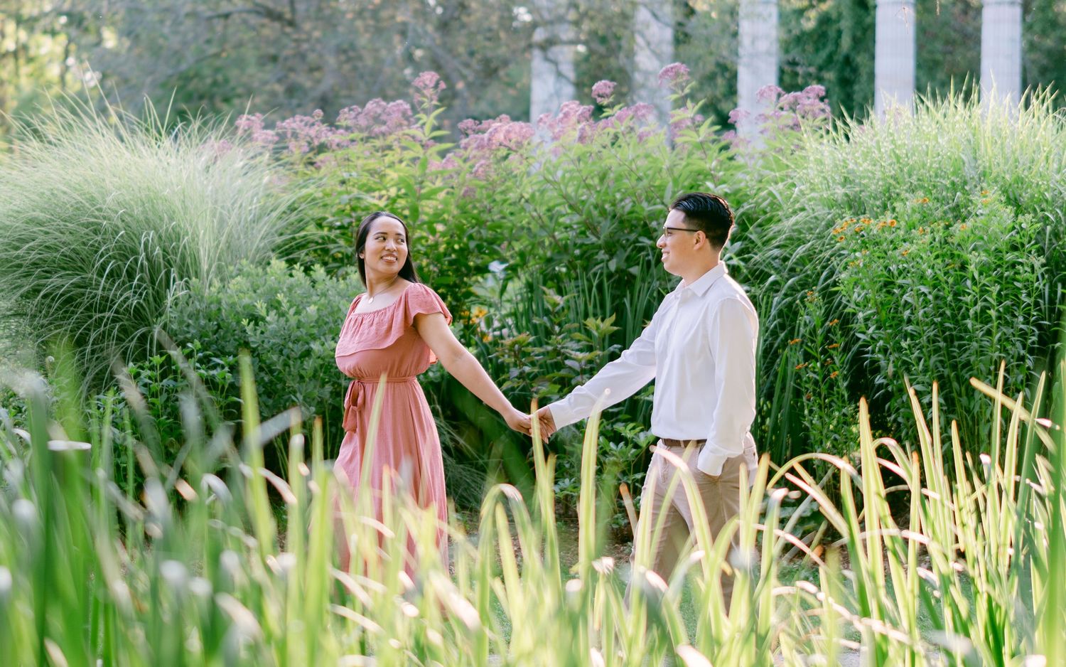 Romantic couple sharing a moment among tall ornamental grasses and pink flowers.