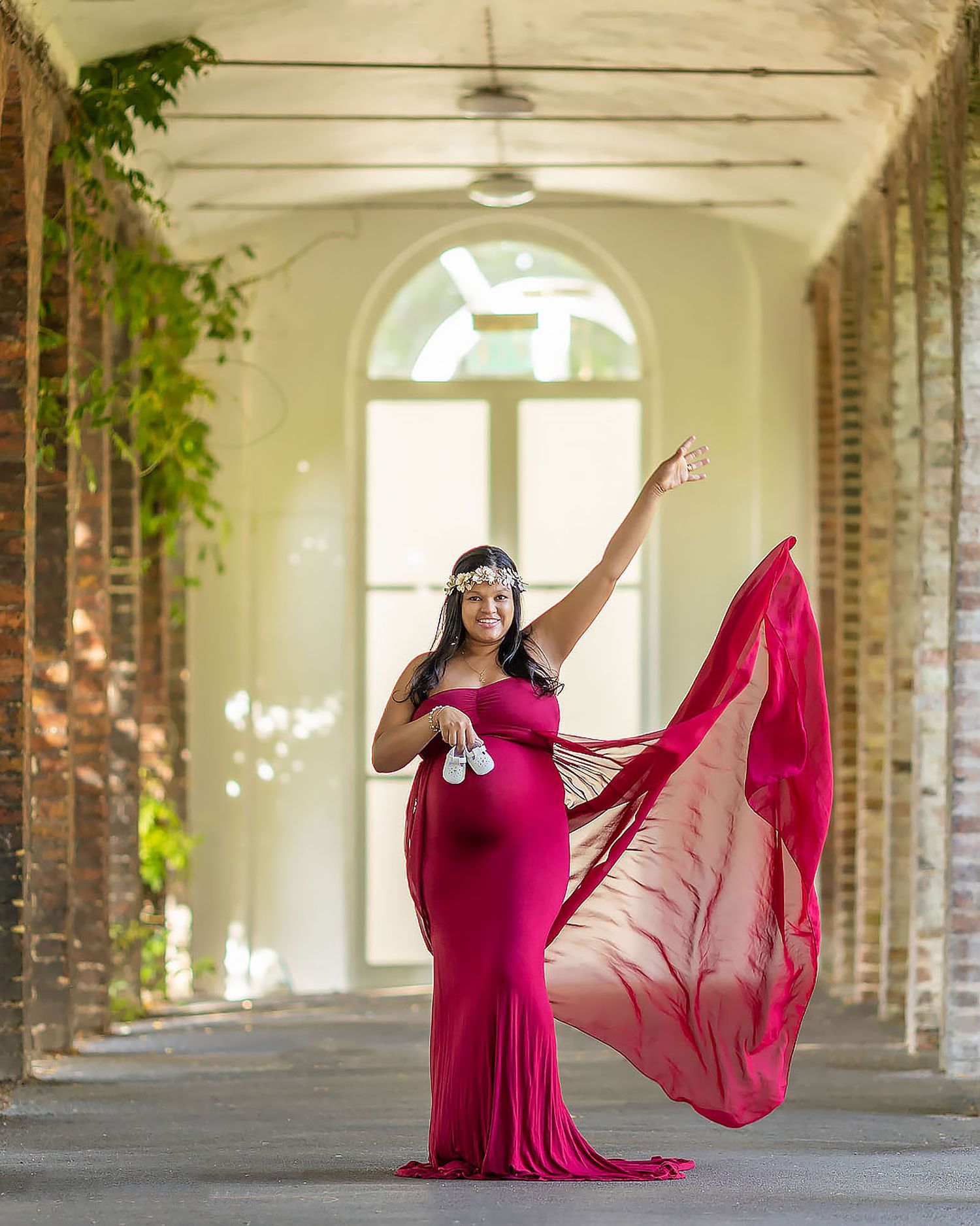 A person in a flowing magenta gown poses dramatically in an arched hallway with natural light and brick columns.
