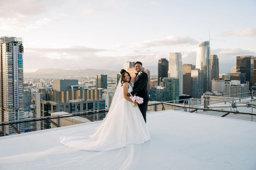 A bride and groom share an intimate moment on a rooftop with the downtown Los Angeles skyline at sunset.