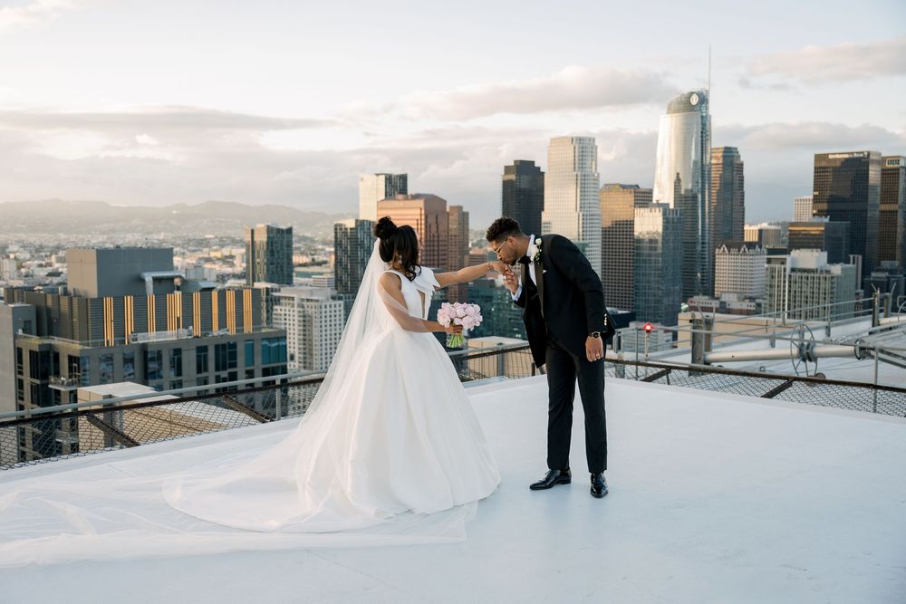 A bride and groom share a romantic moment on a rooftop with the Seattle skyline at sunset in the background.