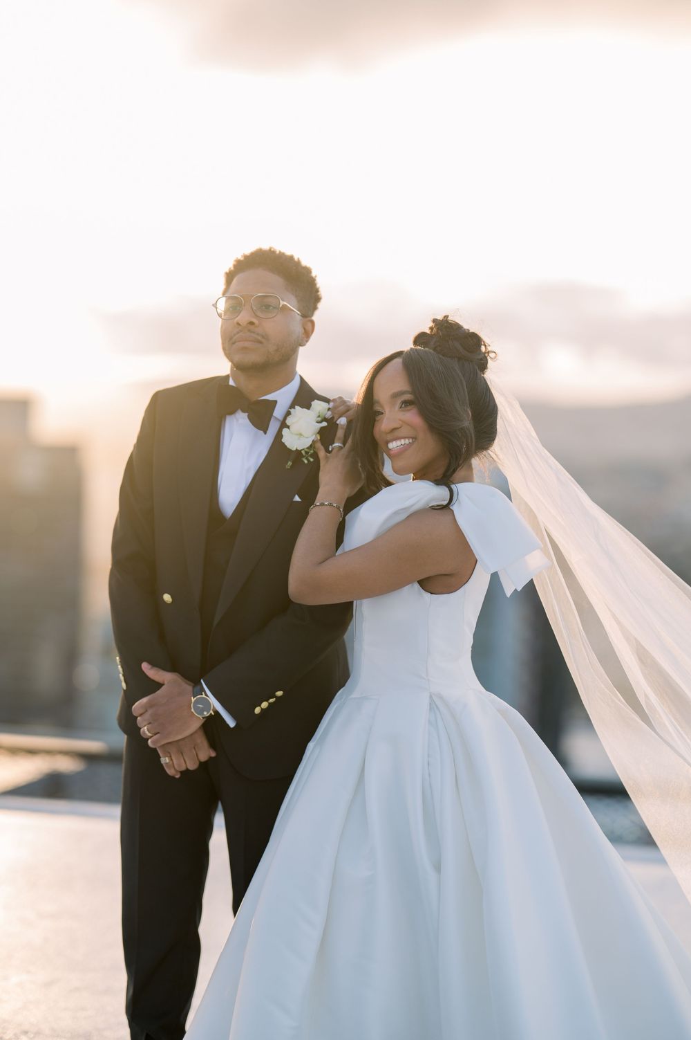 A happy couple in wedding attire share a joyful moment together during golden hour on a city rooftop.