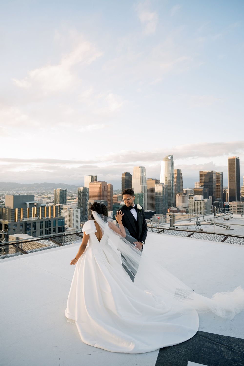A bride and groom share an intimate moment on a rooftop with the Los Angeles skyline during sunset.