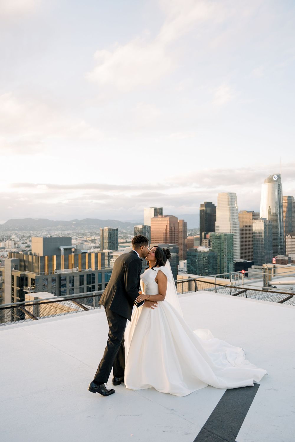 A couple shares a romantic moment on a rooftop overlooking the Los Angeles city skyline at sunset.