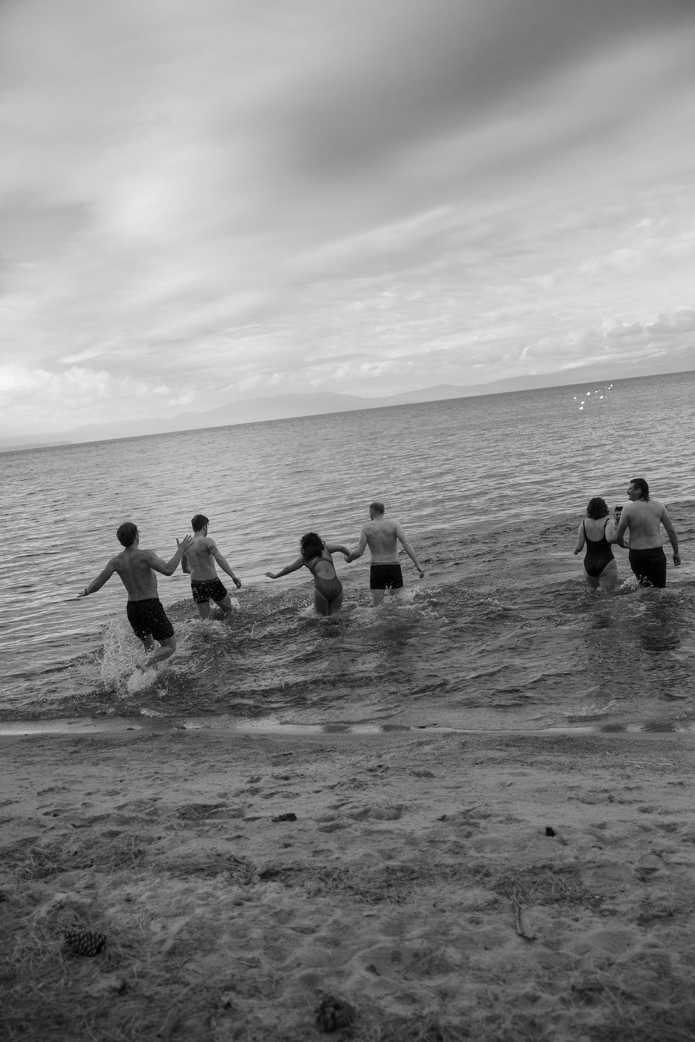 Black and white photo of people running into ocean water together.
