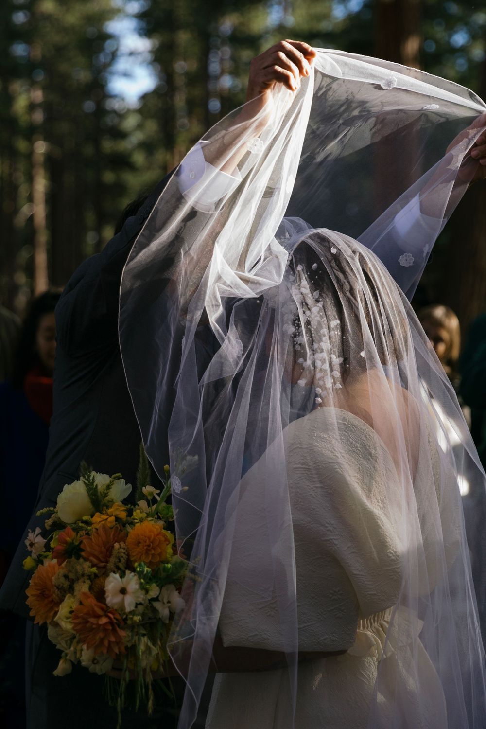 Close-up of flowing white wedding veil and orange bouquet against forest backdrop.
