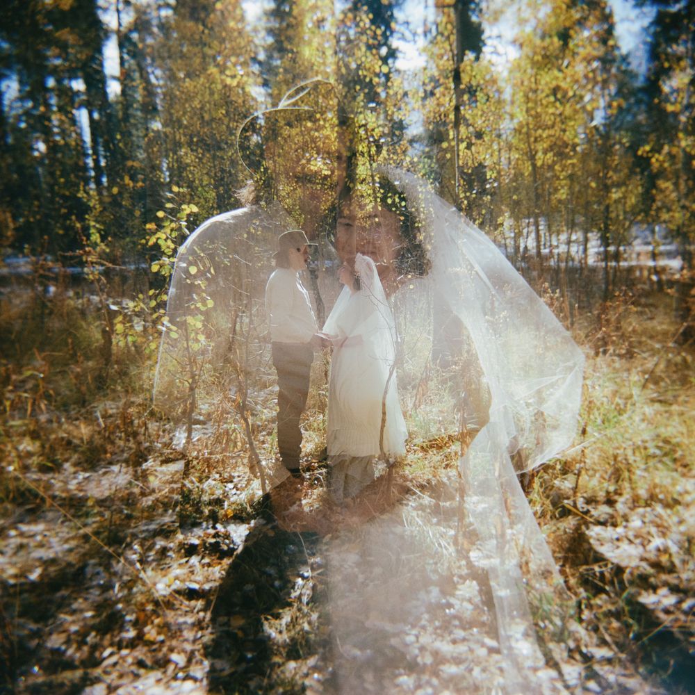 A dreamy double-exposed wedding photograph capturing a couple's intimate moment in a sun-dappled forest.