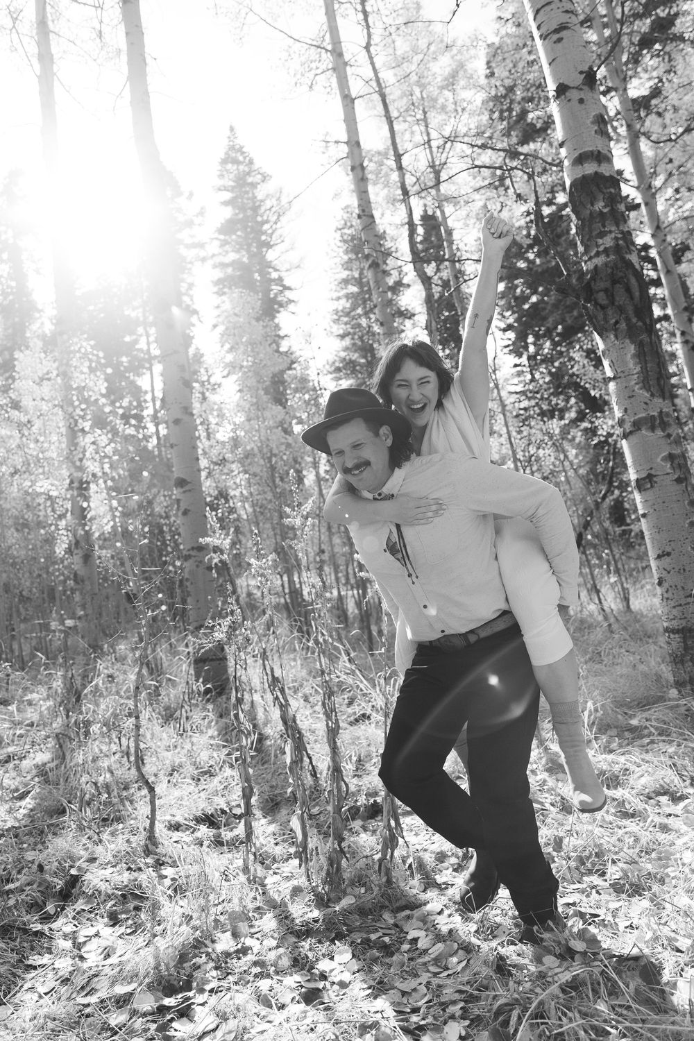 A playful black and white wedding photo showing a couple enjoying a piggyback ride in an aspen grove.