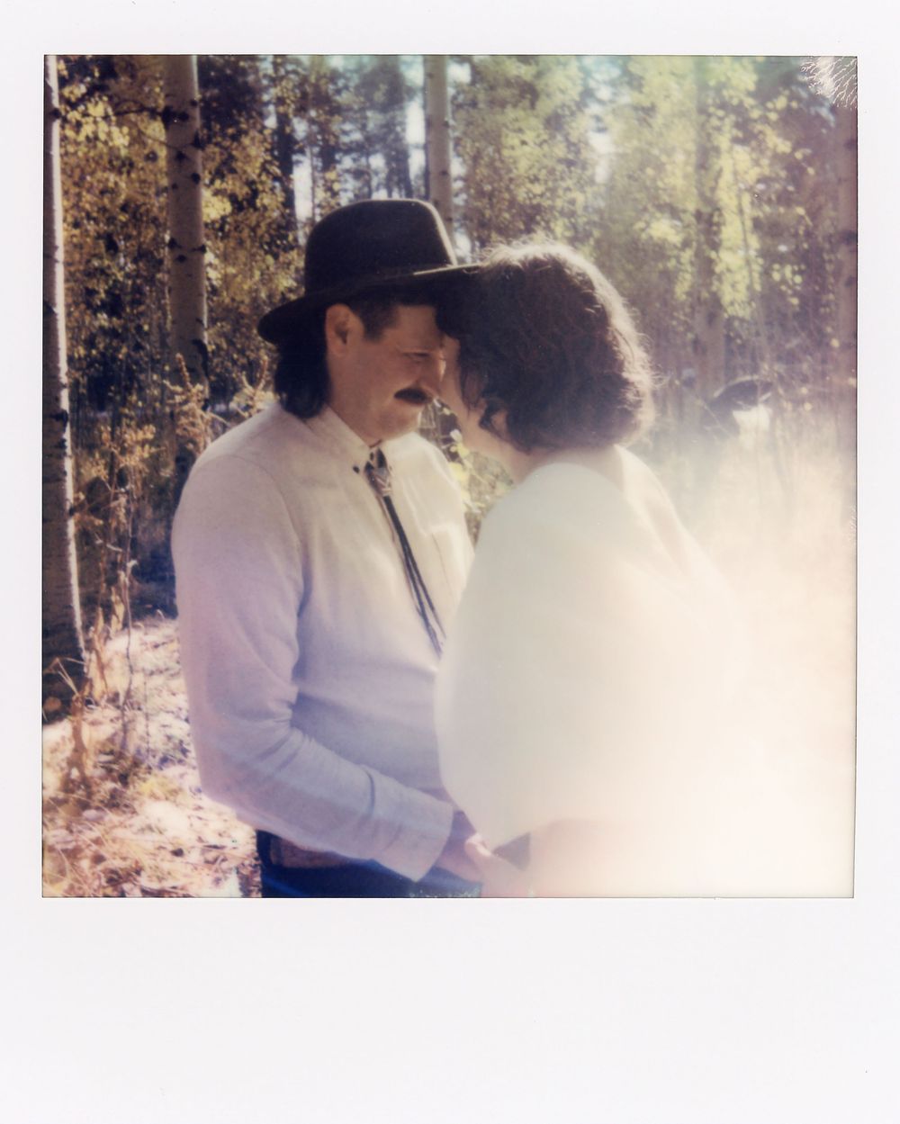 Vintage polaroid style photo of couple sharing intimate moment in sunlit forest.