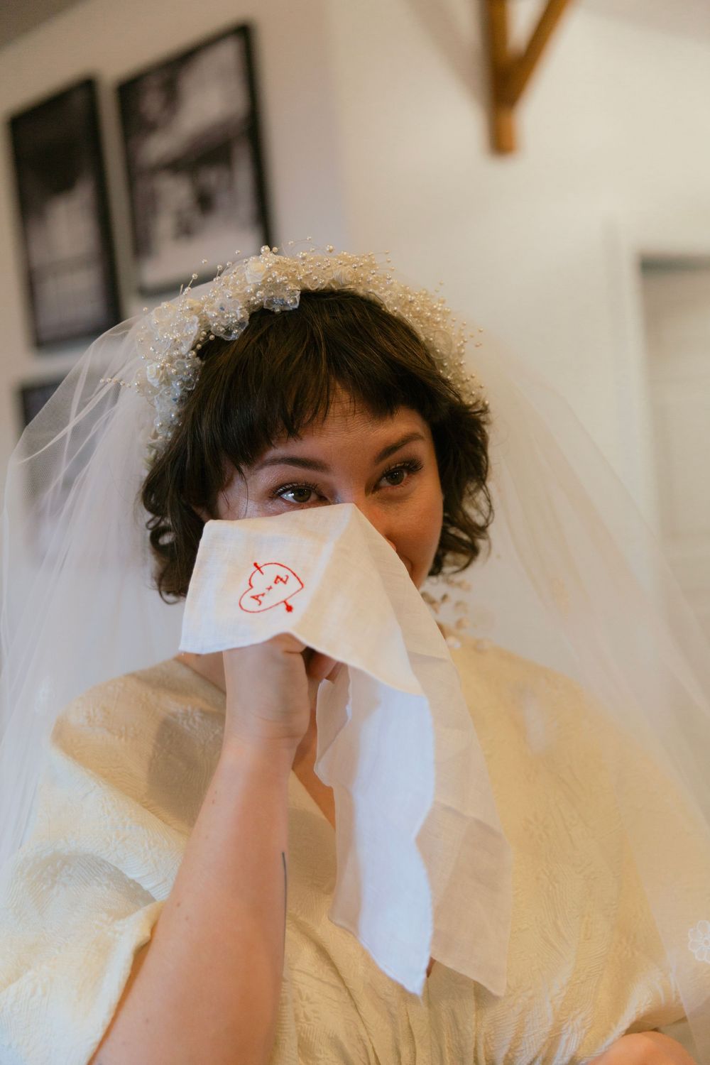 Playful bridal portrait with tissue paper held up to nose beneath wedding veil.