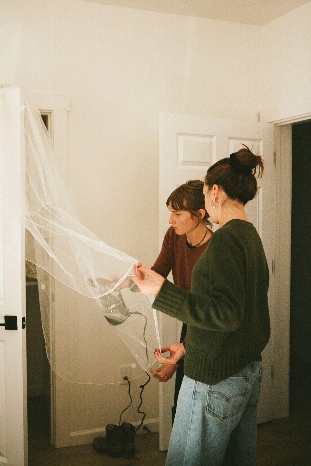 Two people in casual attire adjusting decorative tulle or netting in an indoor setting.