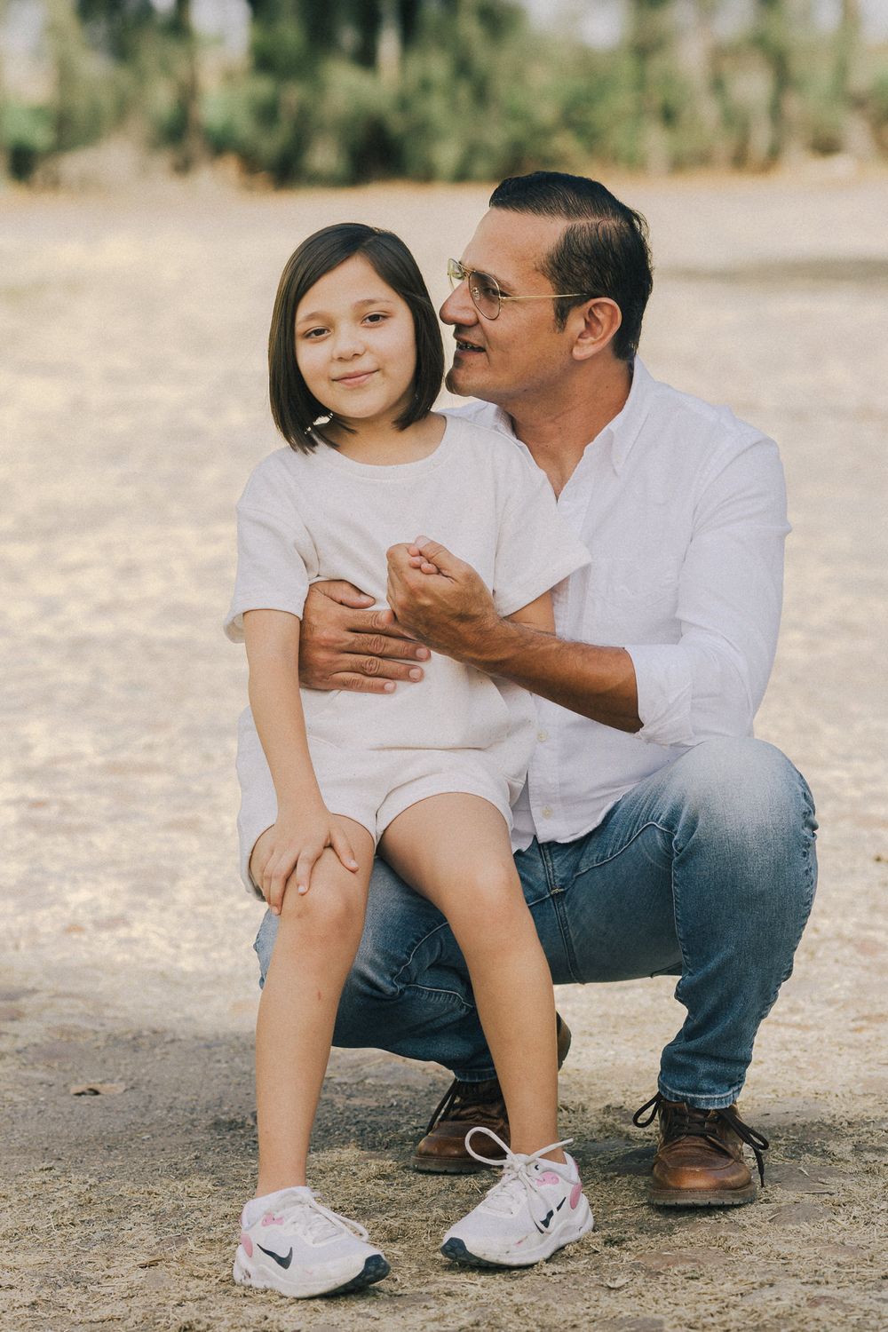 A sweet candid portrait of a parent and child sitting together outdoors wearing white shirts on a sunny day.