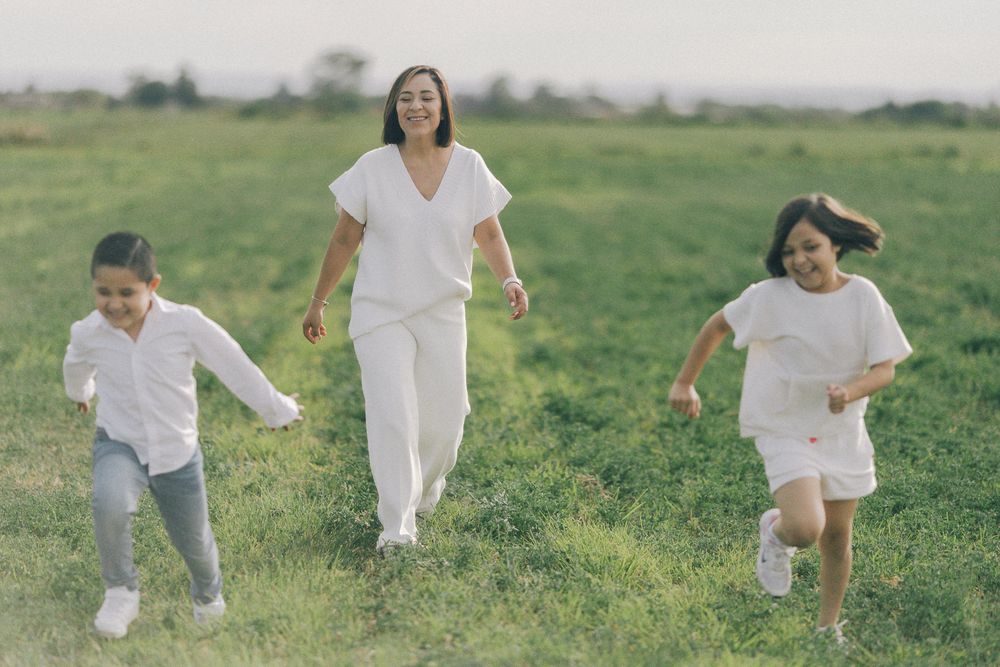 People wearing white clothing run and play together in a grassy field during a sunny day.