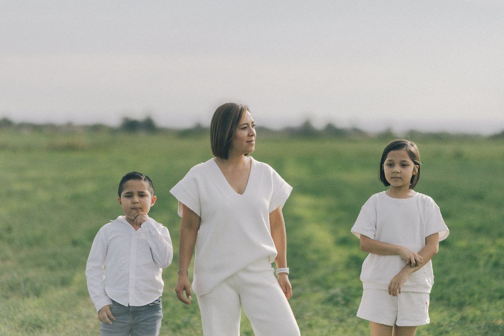 Three people in white clothing walking together on a grassy field at dusk.