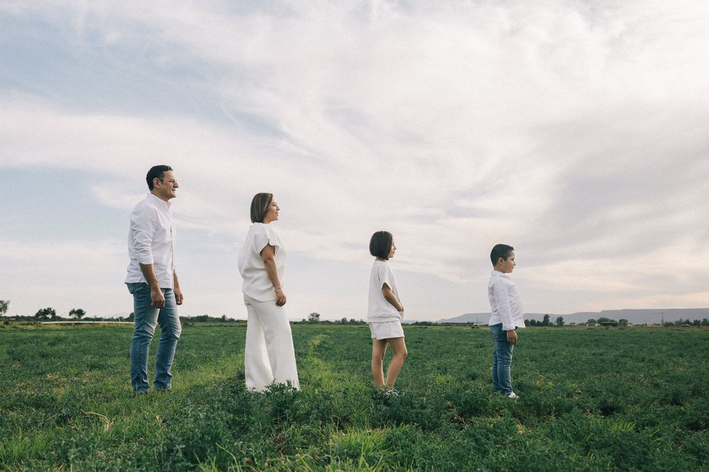 A family stands in a row on a grassy hill overlooking a scenic landscape on a cloudy day.