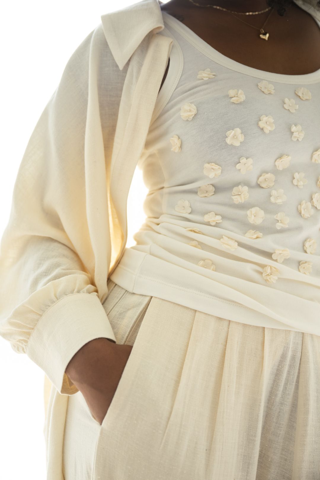 Close-up of cream colored outfit with floral applique details and gathered waist.